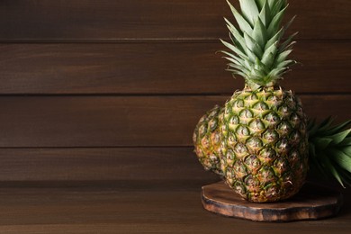 Photo of Whole ripe pineapples on wooden table, space for text