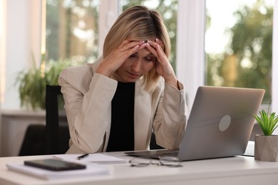 Overwhelmed woman sitting at table with laptop in office