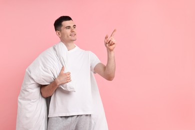Photo of Happy man in pyjama holding blanket on pink background, space for text