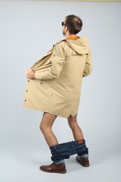 Photo of Exhibitionist exposing naked body under coat on light background, back view