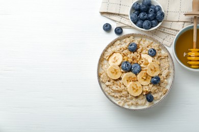 Tasty oatmeal with banana, blueberries, walnuts and honey served in bowl on white wooden table, flat lay. Space for text