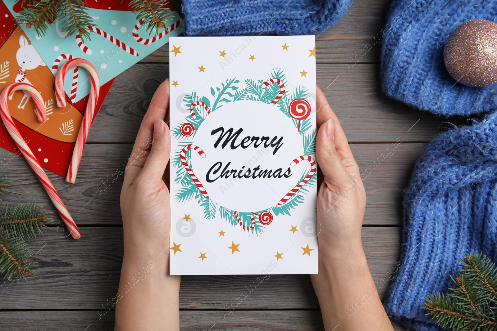 Photo of Woman holding Christmas card at grey wooden table, top view