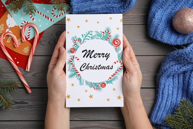 Woman holding Christmas card at grey wooden table, top view