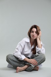Beautiful young woman sitting on grey background