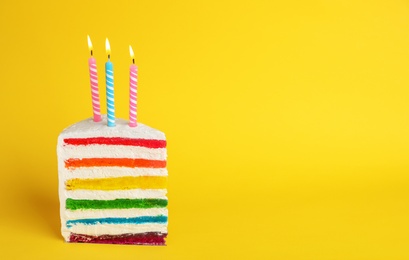 Photo of Slice of delicious rainbow cake with candles on color background