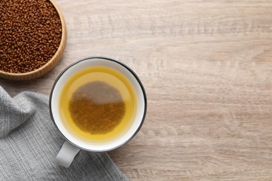 Photo of Buckwheat tea in cup and bowl with granules on wooden table, flat lay. Space for text