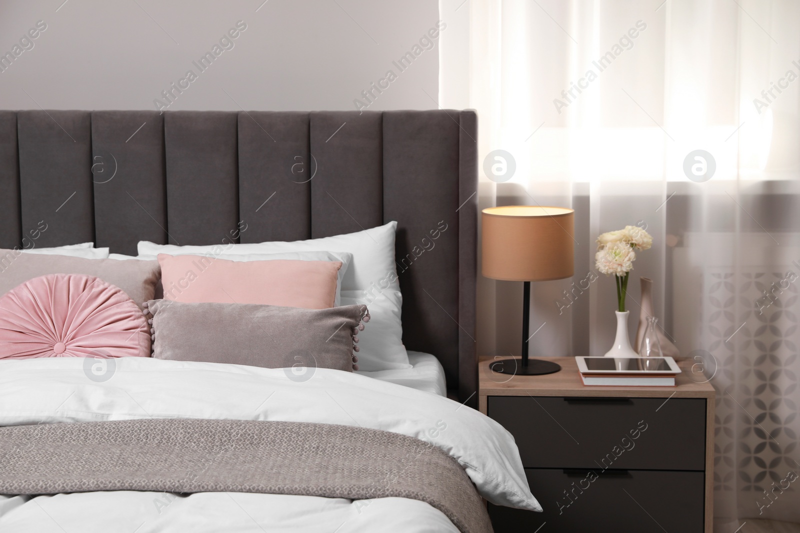 Photo of Comfortable bed with cushions, lamp and different decor on bedside table in room. Stylish interior