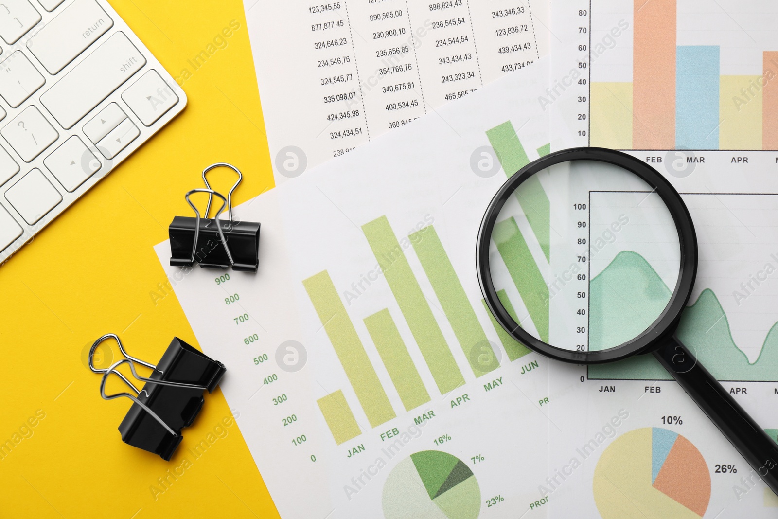 Photo of Accounting documents, magnifying glass, computer keyboard and binder clips on yellow background, flat lay