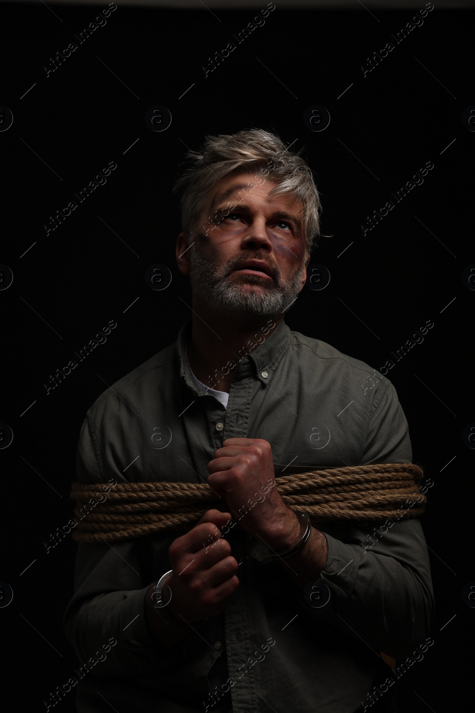 Photo of Beaten man tied with rope on black background. Hostage taking