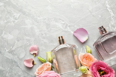 Photo of Flat lay composition of different perfume bottles and flowers on light grey marble background, space for text