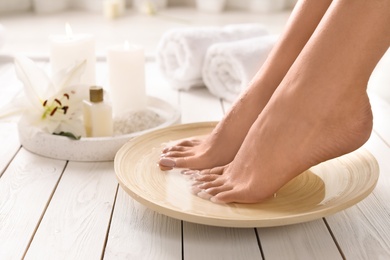 Closeup view of woman soaking her feet in dish with water on wooden floor, space for text. Spa treatment