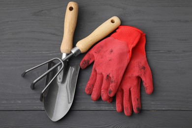 Gardening gloves, trowel and rake on grey wooden table, top view