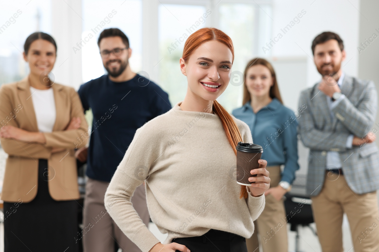Photo of Portrait of happy businesswoman with paper cup and her team in office