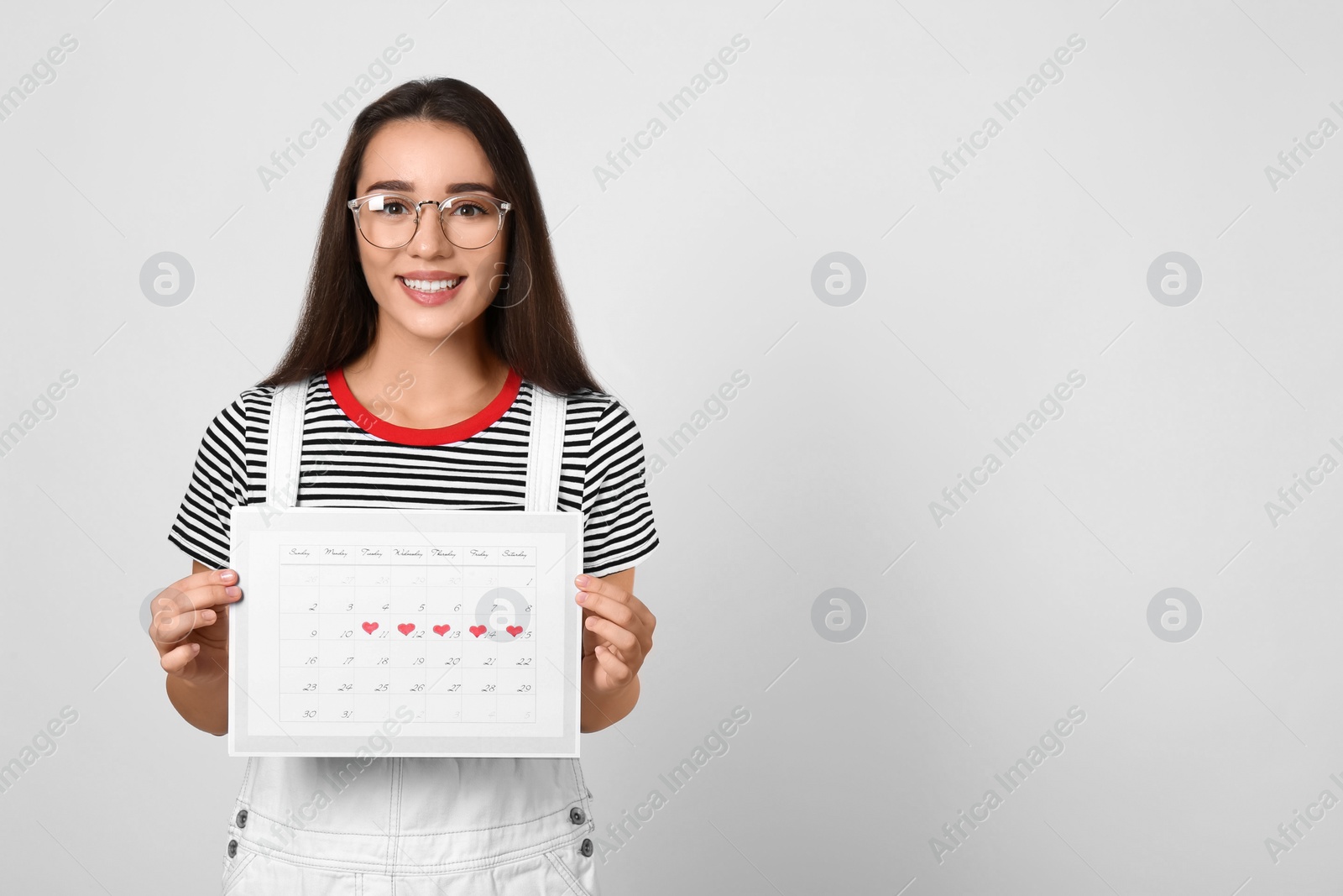 Photo of Young woman holding calendar with marked menstrual cycle days on light background. Space for text