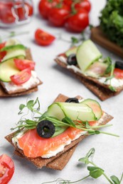Photo of Tasty rye crispbreads with salmon, cream cheese and vegetables on light grey table
