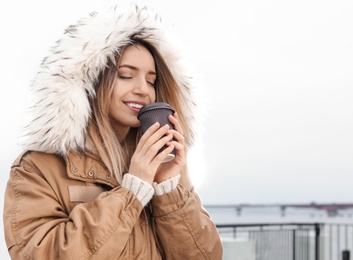 Photo of Young woman with cup of coffee walking outdoors. Space for text