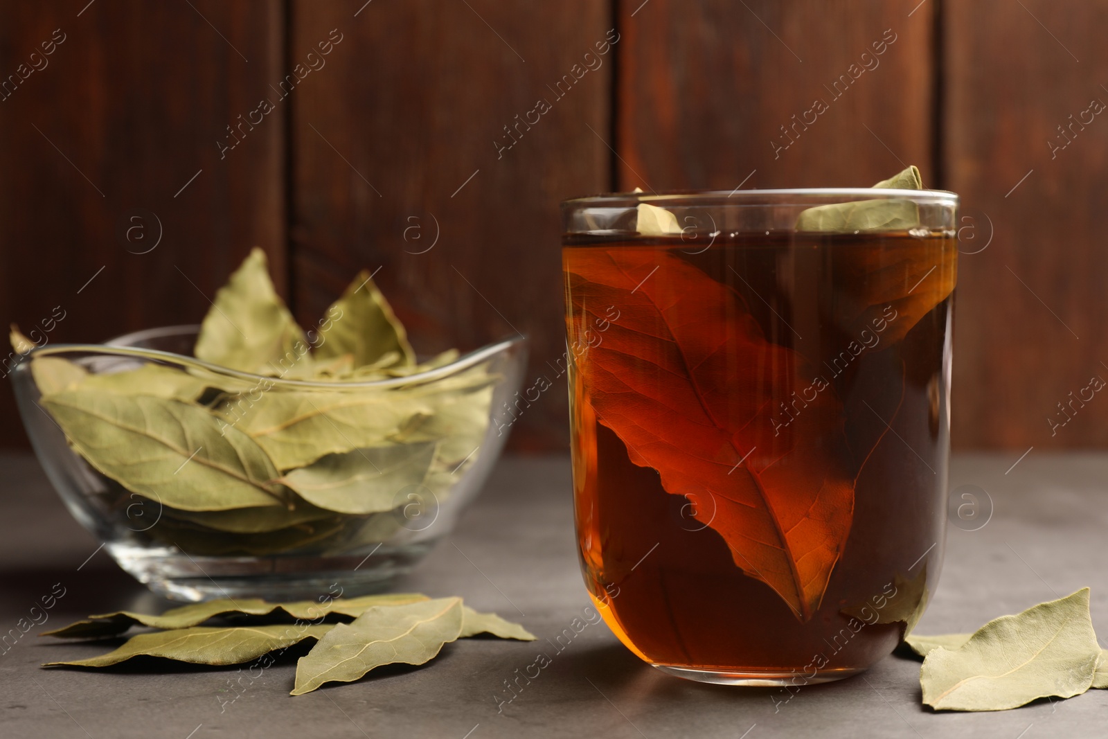 Photo of Cup of freshly brewed tea with bay leaves on grey table. Space for text