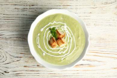 Photo of Delicious broccoli cream soup with croutons served on white wooden table, top view