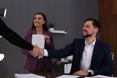 Photo of Businessman and client shaking hands over table with documents in office