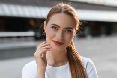 Photo of Portrait of beautiful young woman with red hair outdoors. Attractive lady smiling and looking into camera