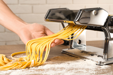 Photo of Woman preparing noodles with pasta maker machine at wooden table, closeup