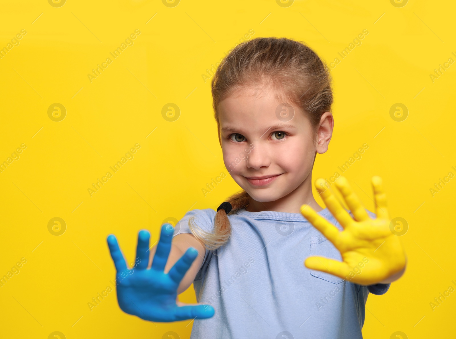 Photo of Little girl with hands painted in Ukrainian flag colors on yellow background, space for text. Love Ukraine concept