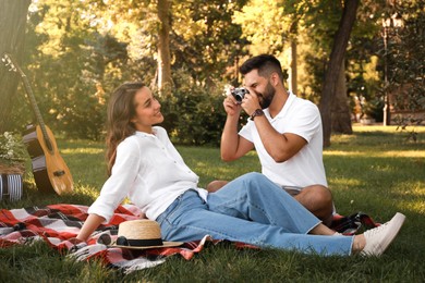 Photo of Man taking picture of his girlfriend on picnic plaid in summer park