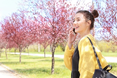 Young woman talking by phone outdoors on sunny day