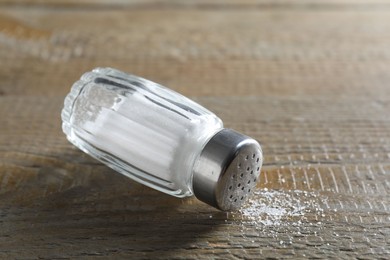 Photo of Organic salt in glass shaker on wooden table, closeup. Space for text