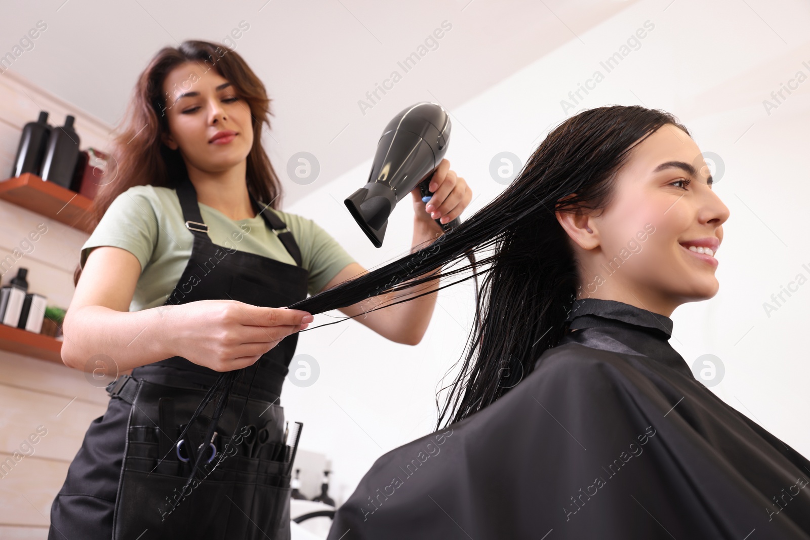 Photo of Hairdresser drying woman's hair in beauty salon