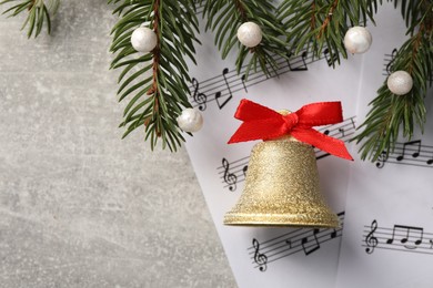 Golden shiny bell with red bow, music sheets and fir branches on light gray table, flat lay. Space for text. Christmas decoration