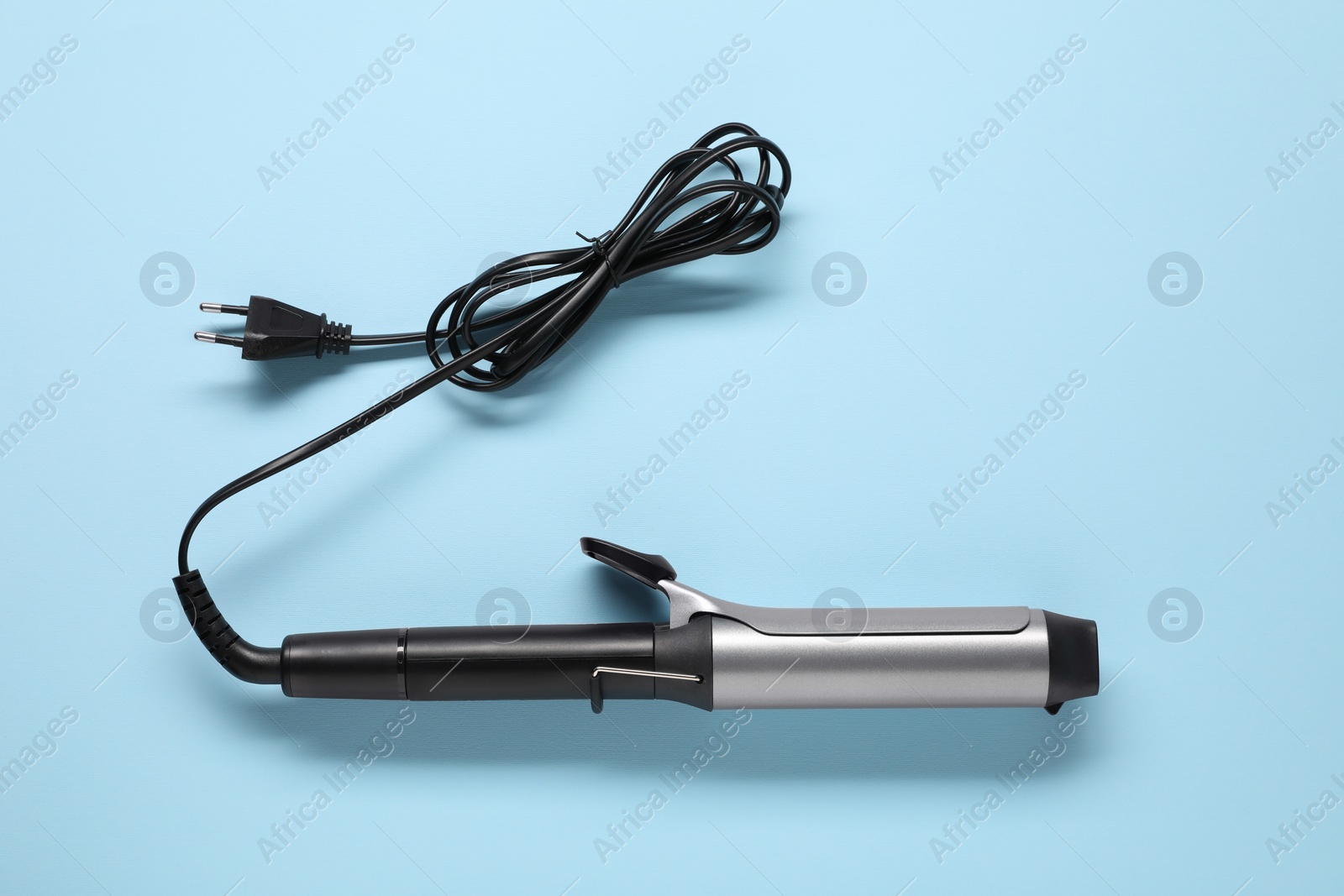 Photo of One curling iron on light blue background, top view. Hair styling appliance