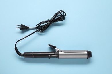 One curling iron on light blue background, top view. Hair styling appliance