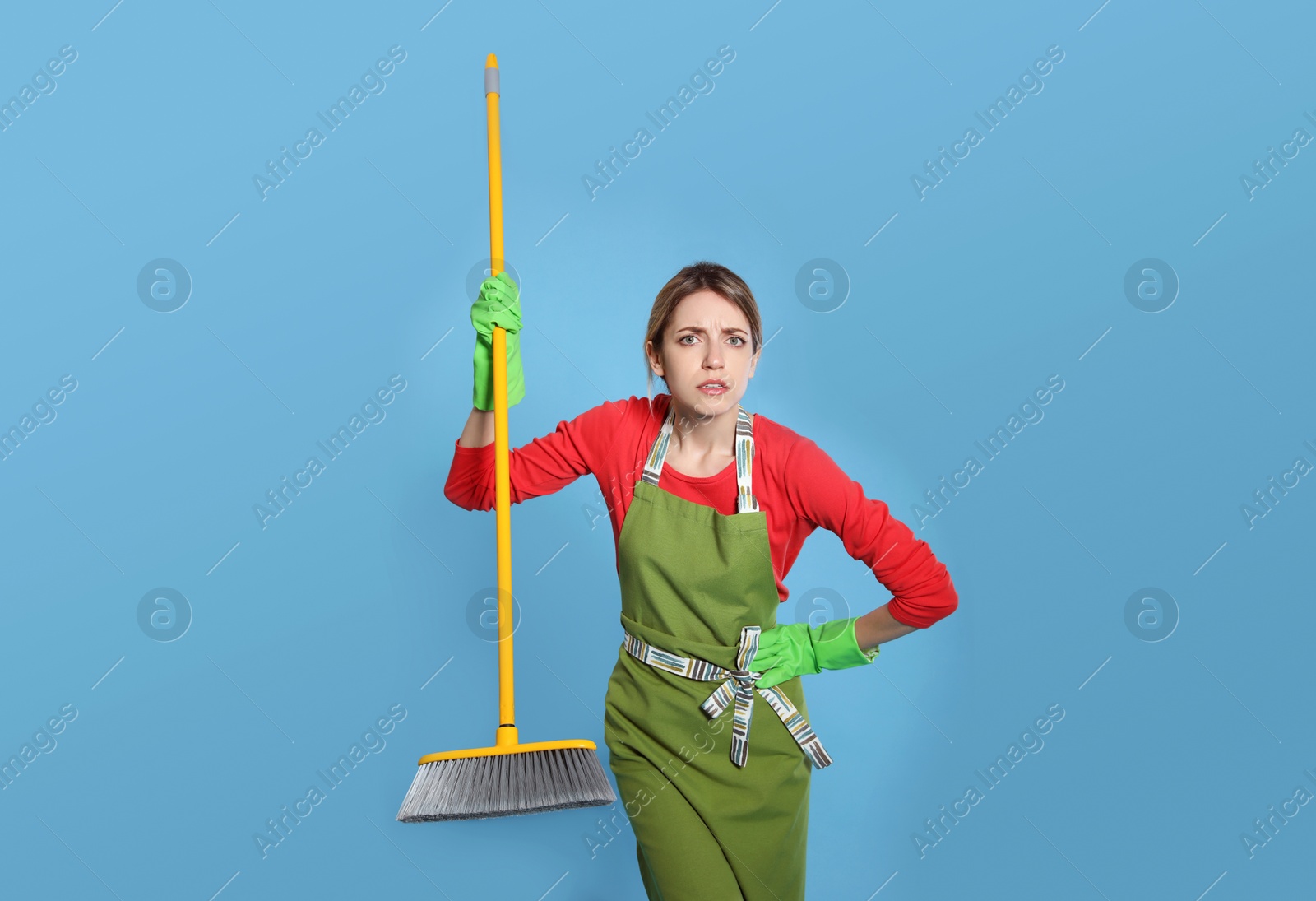 Photo of Young housewife with broom on light blue background