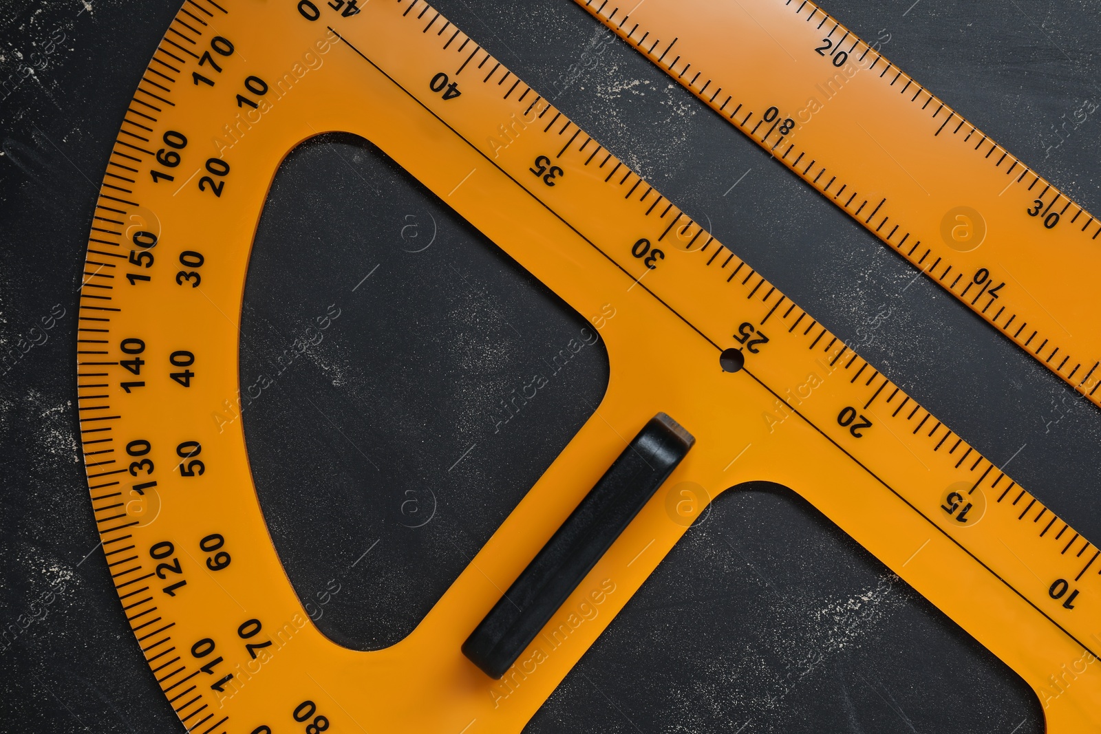 Photo of Ruler and protractor with measuring length and degree markings on blackboard, flat lay