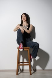 Photo of Smiling tattooed woman sitting on stool against light background