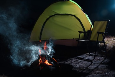 Beautiful bonfire and folding chair near camping tent outdoors at night