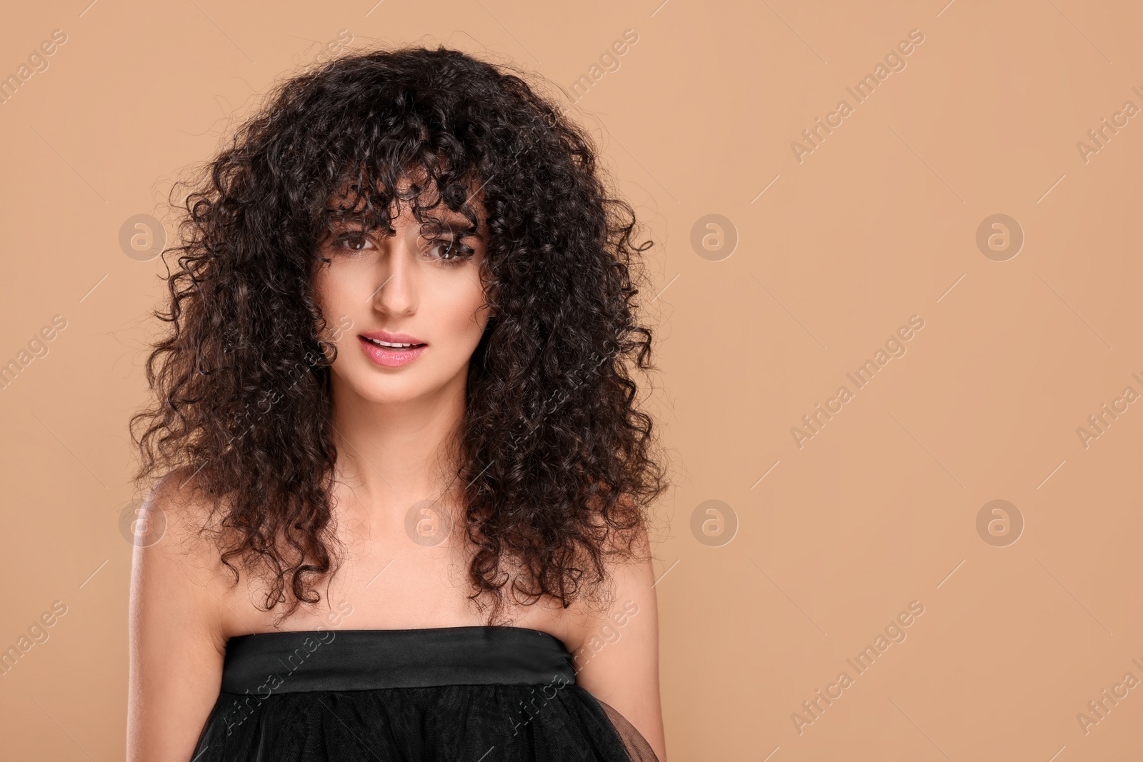 Photo of Beautiful young woman with long curly hair on beige background. Space for text
