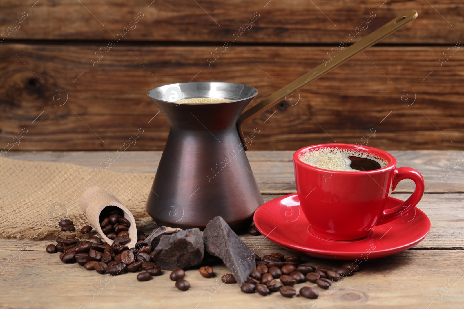 Photo of Hot turkish coffee pot, cup of drink, beans and chocolate on wooden table