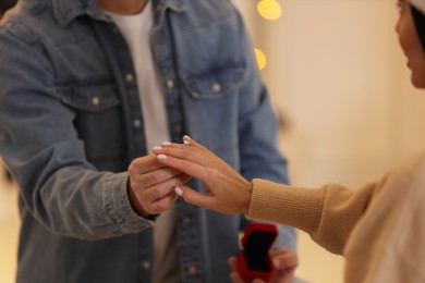 Making proposal. Man putting engagement ring on his girlfriend's finger against blurred background, closeup