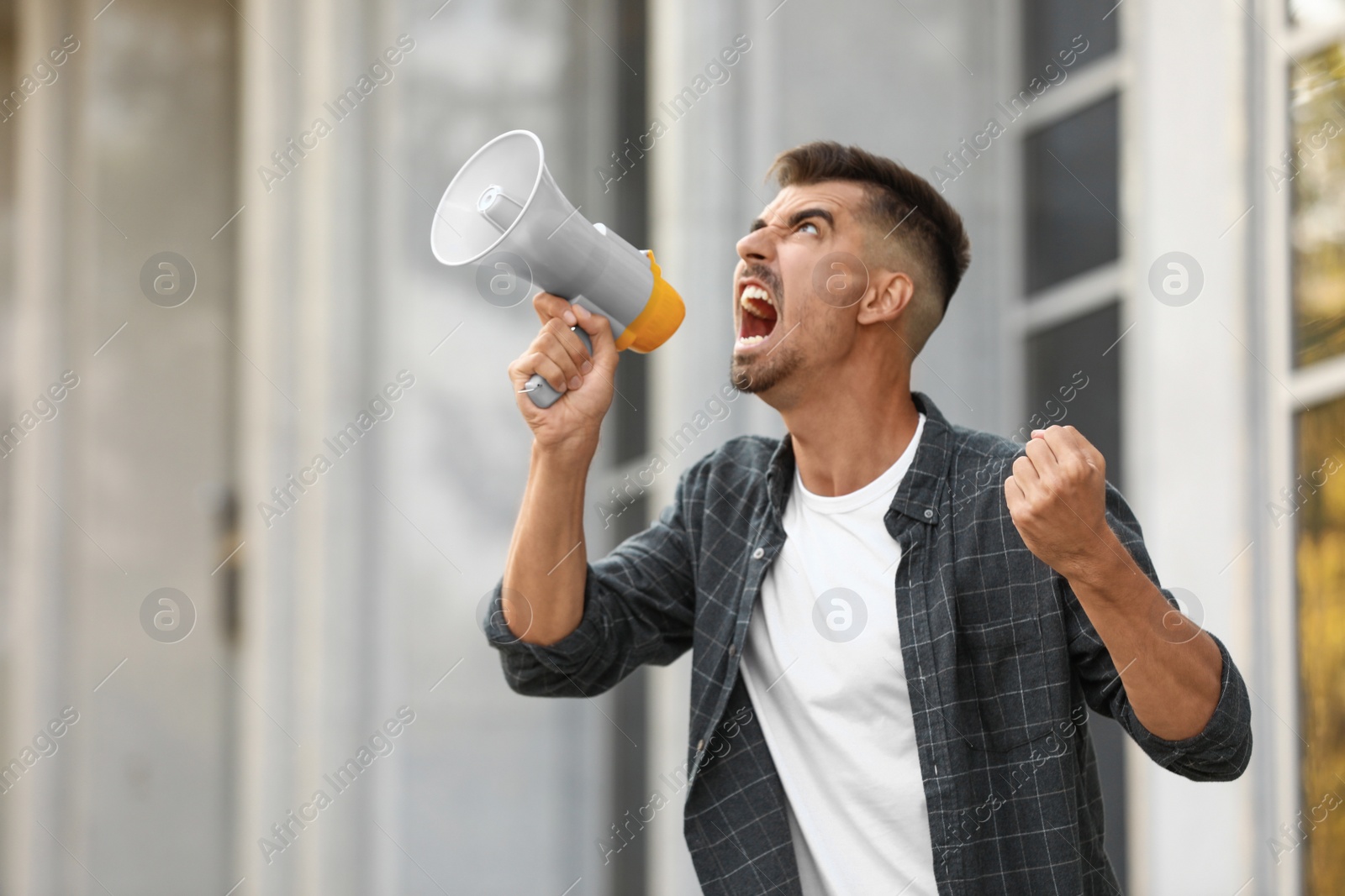 Image of Emotional young man with megaphone outdoors. Protest leader