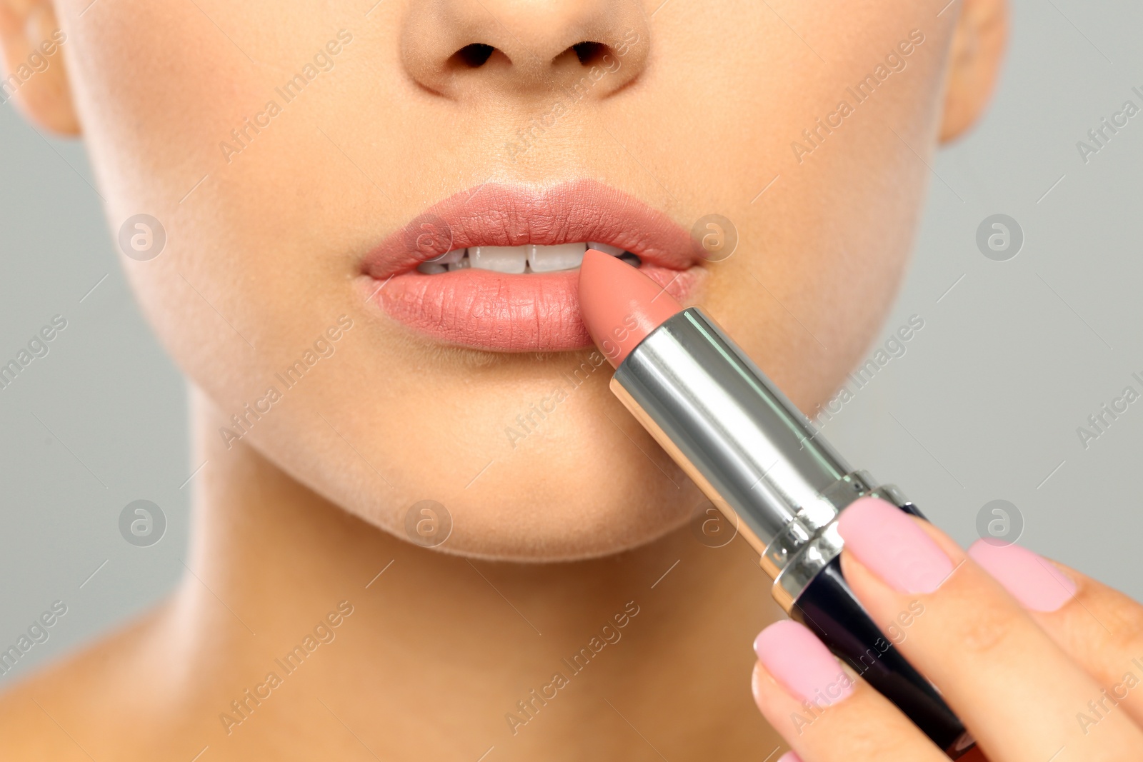 Photo of Young woman applying lipstick on color background, closeup