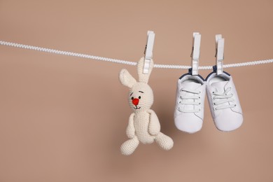 Cute small baby shoes and toy hanging on washing line against brown background, space for text