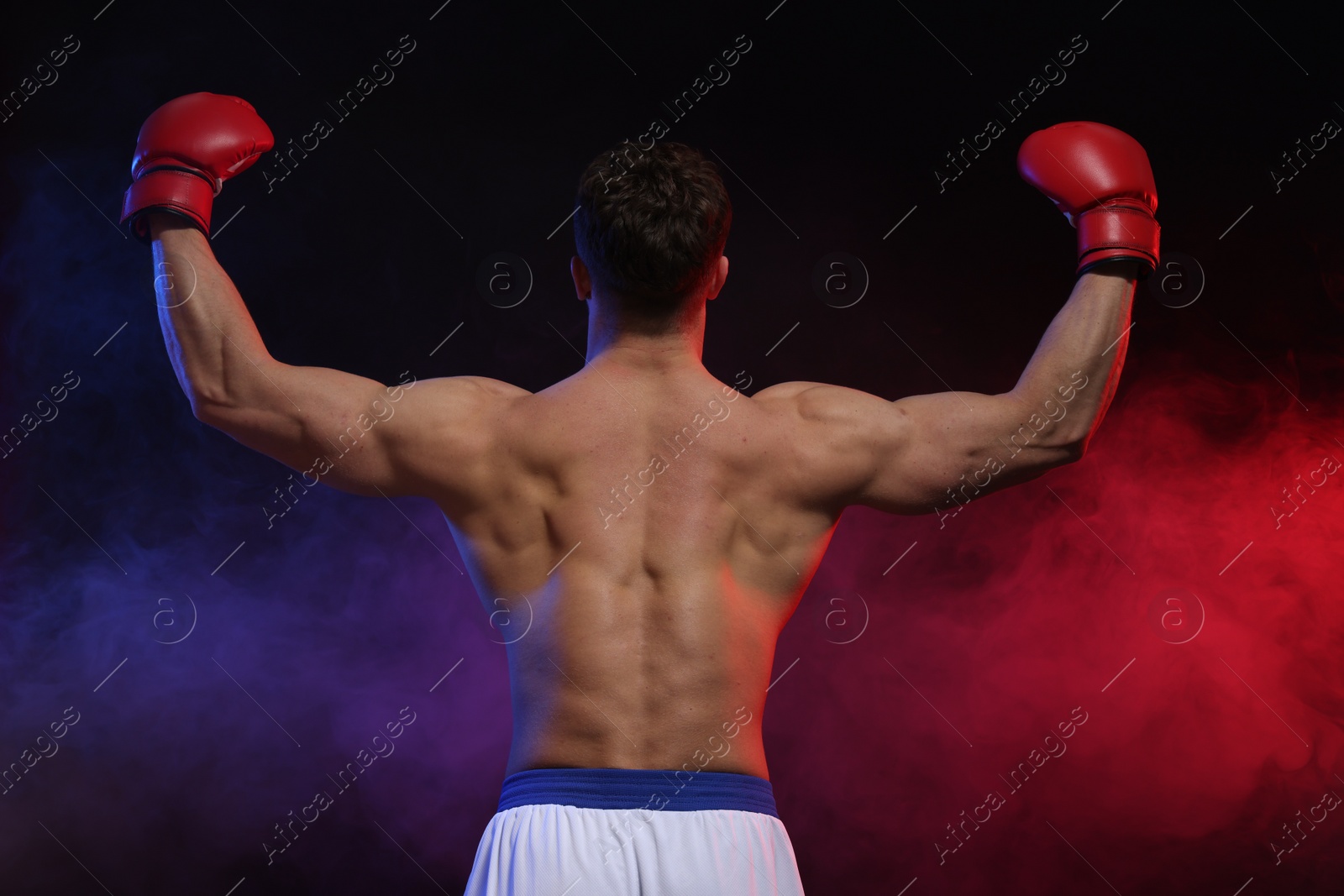 Photo of Man wearing boxing gloves on dark background, back view