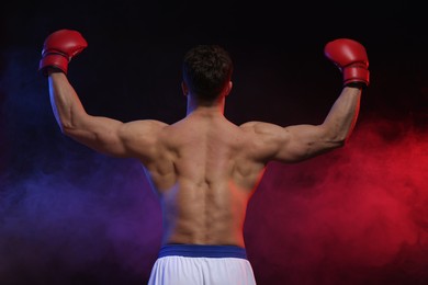 Photo of Man wearing boxing gloves on dark background, back view