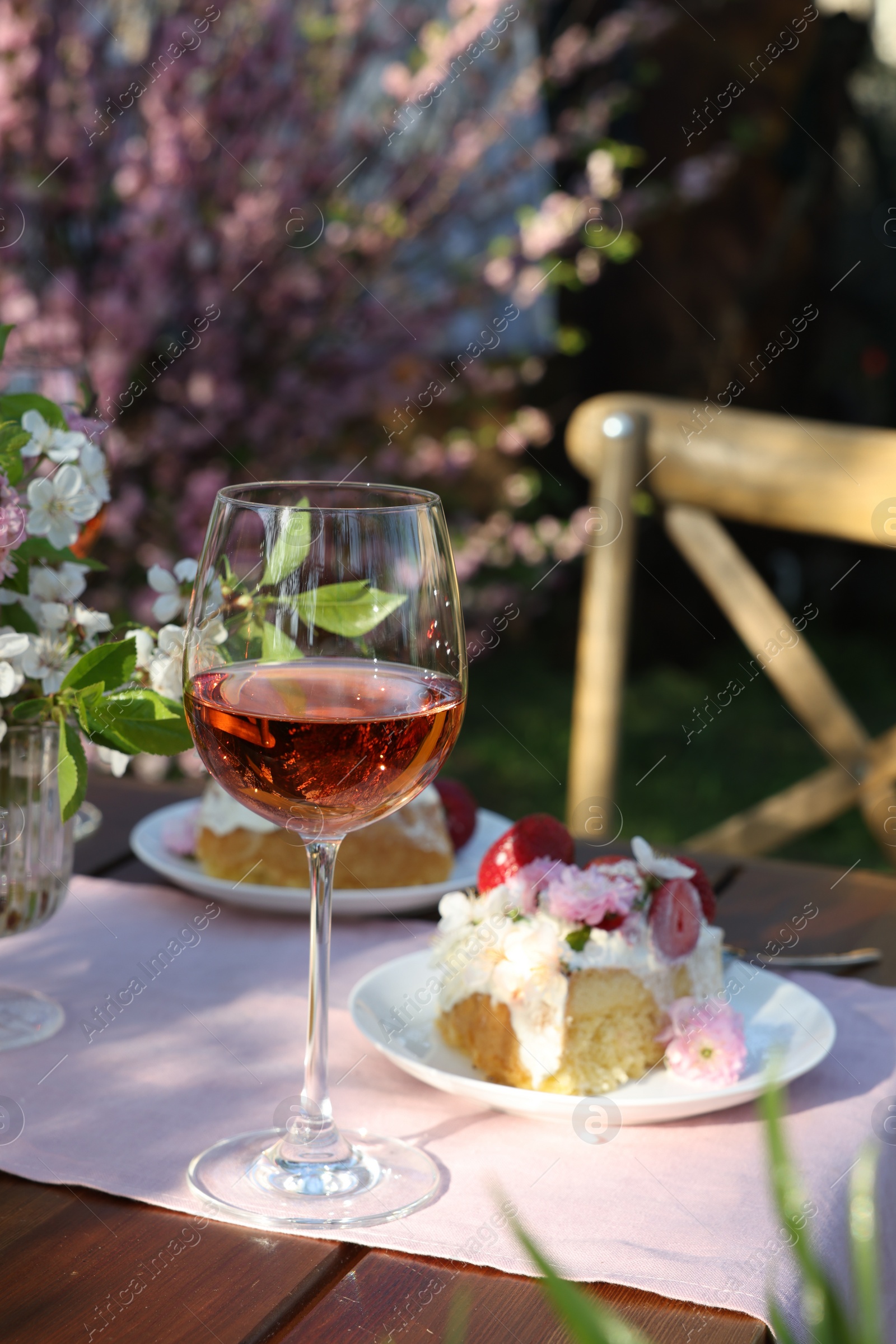 Photo of Vase with spring flowers, wine and cake on table served for romantic date in garden