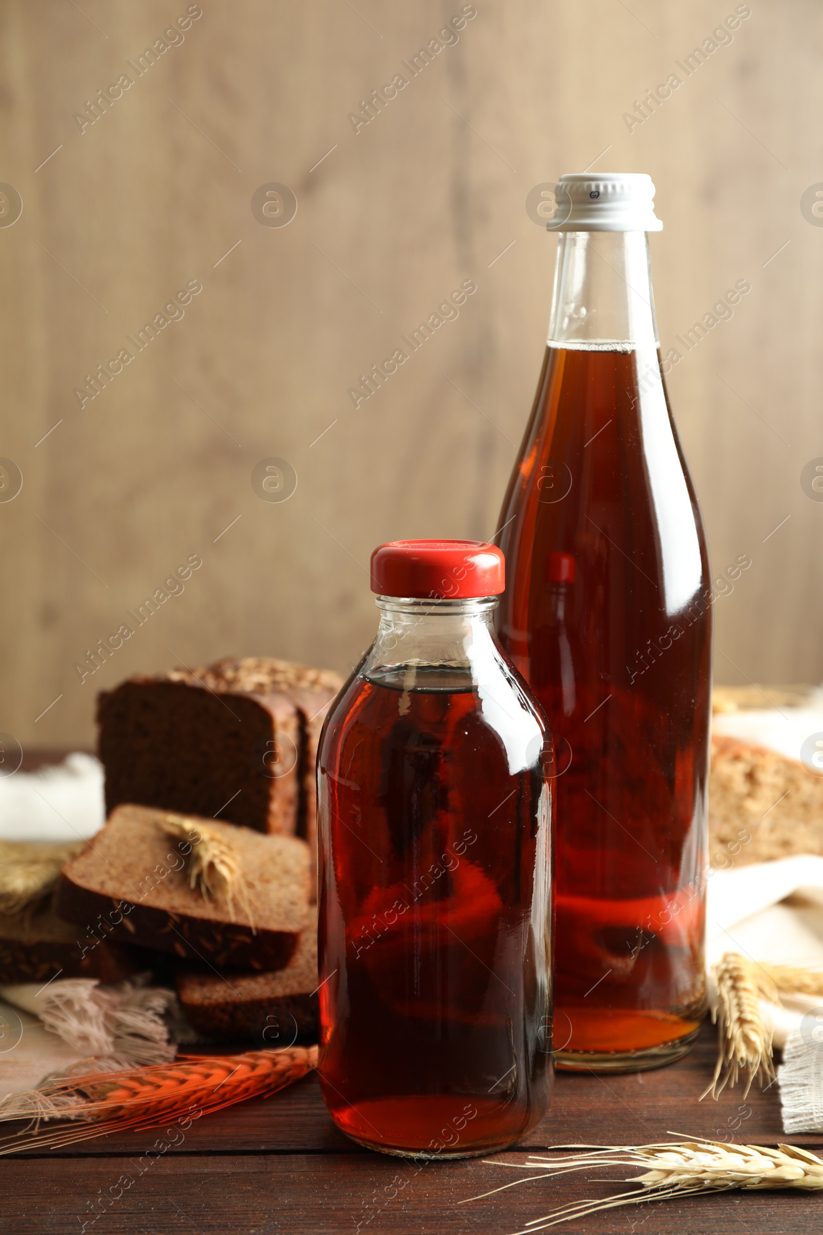 Photo of Bottles of delicious fresh kvass, spikelets and bread on wooden table