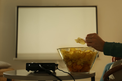 Photo of Man eating chips while watching movie using video projector at home, closeup