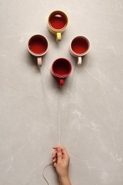Photo of Woman holding threads with cups like balloons on beige marble background, top view
