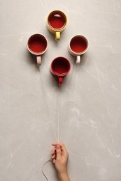 Woman holding threads with cups like balloons on beige marble background, top view